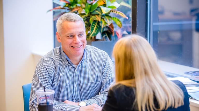 Photo of Brian Dudt sitting at a table talking to a colleague